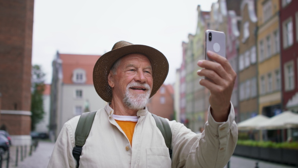 A portrait of happy senior man tourists taking selfie outdoors in historic town