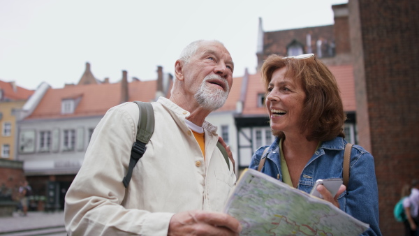 A happy senior couple tourists using smartphone and map outdoors in historic town