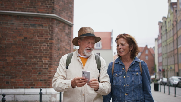 A happy senior couple tourists using smartphone outdoors in historic town