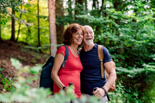 A senior tourist couple with backpacks on a walk in forest in nature.