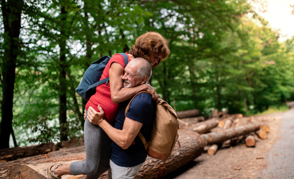 A senior tourist couple with backpacks walking in forest in nature.