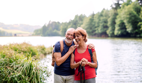 A senior tourist couple on a walk in nature, standing by lake. Copy space.