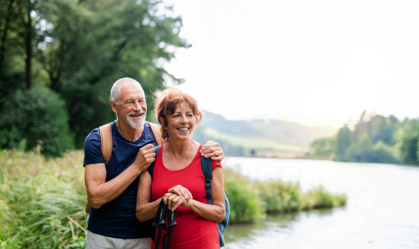 A senior tourist couple on a walk in nature, standing by lake. Copy space.