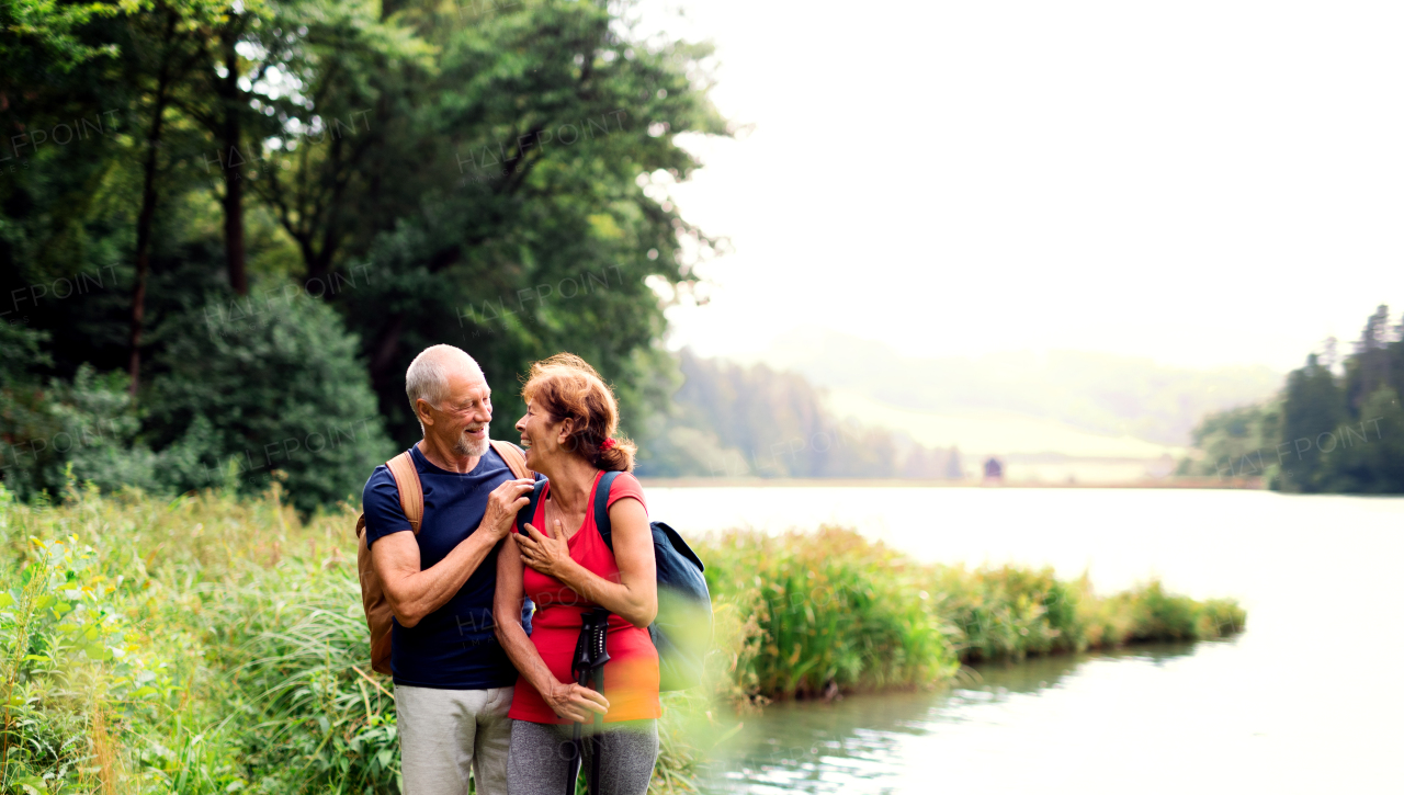 A senior tourist couple on a walk in nature, standing by lake. Copy space.