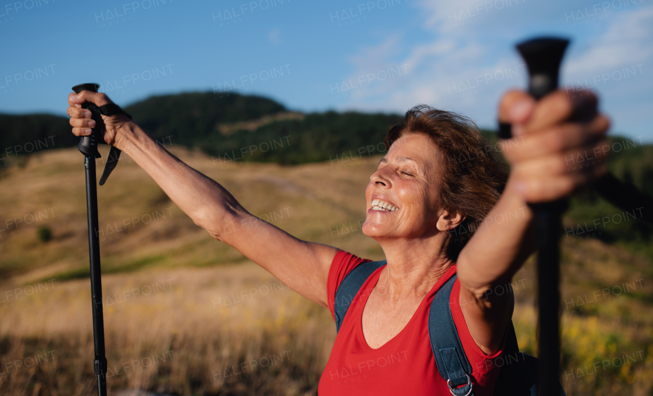 Active senior woman tourist with backpack hiking in nature, resting.