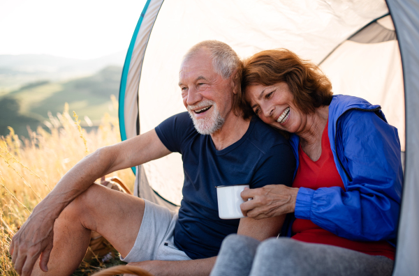 A senior tourist couple in love with shelter sitting in nature at sunset, resting.