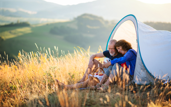 A senior tourist couple in love with shelter sitting in nature at sunset, resting.