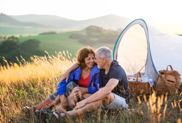 A senior tourist couple in love with shelter sitting in nature at sunset, resting.