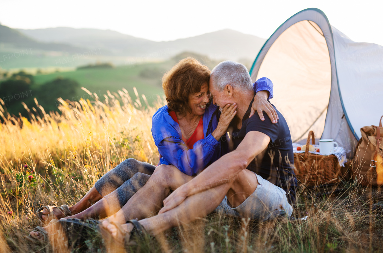 A senior tourist couple in love with shelter sitting in nature at sunset, resting.