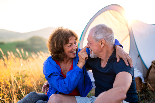 A senior tourist couple in love with shelter sitting in nature at sunset, resting.