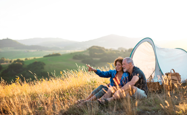 A senior tourist couple in love with shelter sitting in nature at sunset, resting.