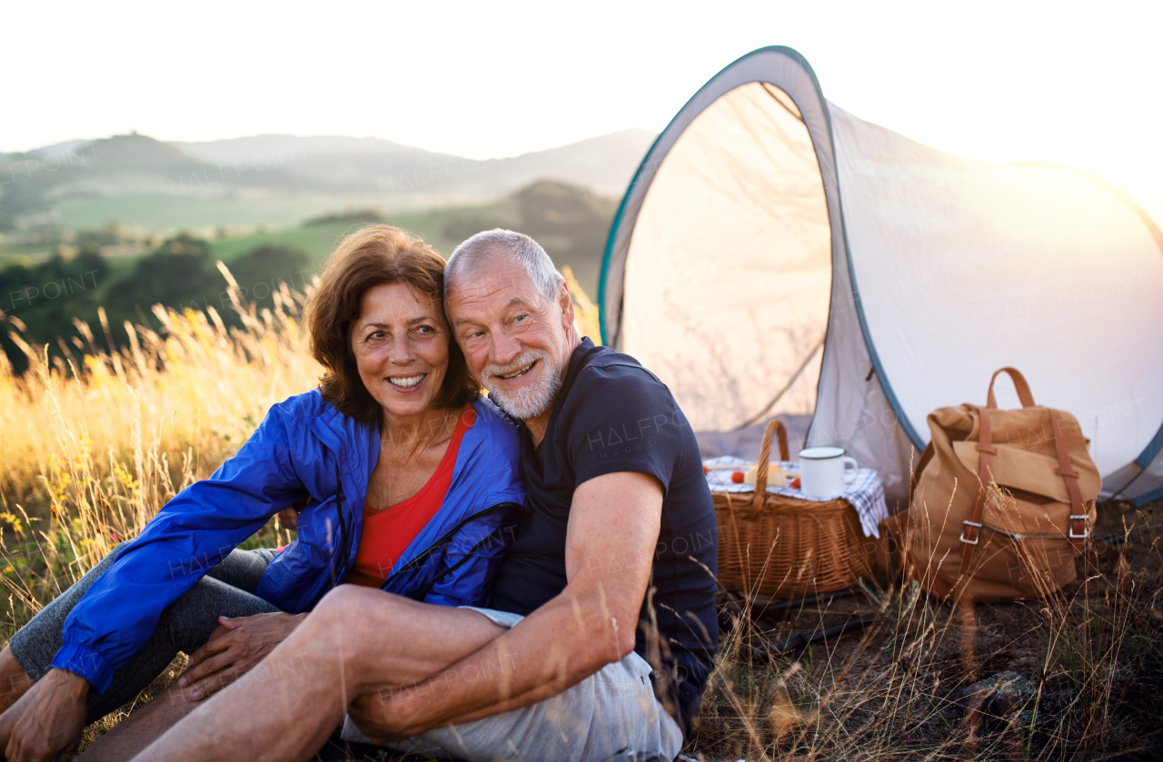 A senior tourist couple in love with shelter sitting in nature at sunset, resting.