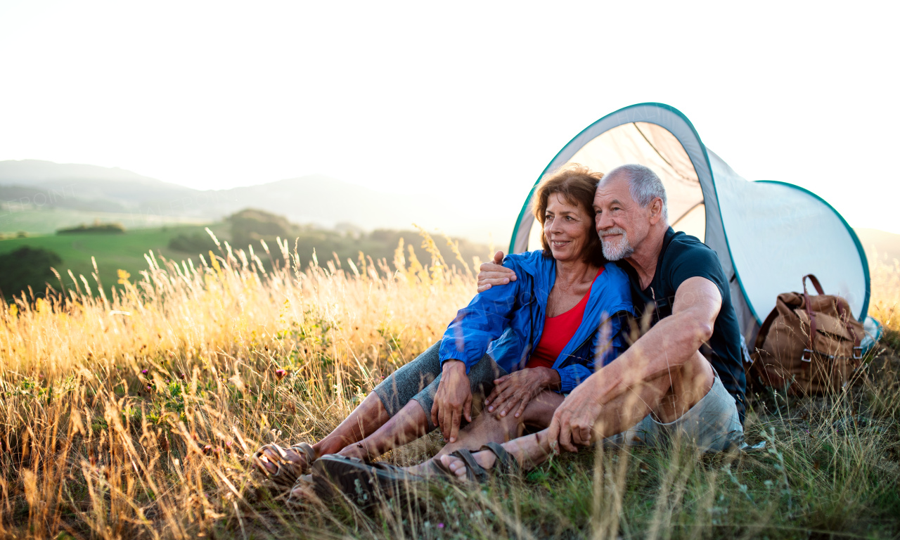 A senior tourist couple in love with shelter sitting in nature at sunset, resting.