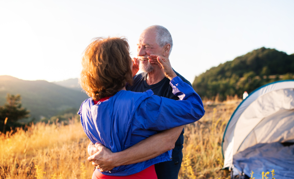 Senior tourist couple in love with shelter standing in nature at sunset, hugging.