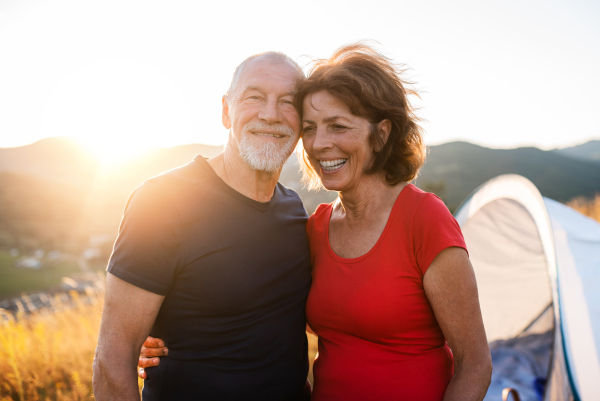 A senior tourist couple standing in nature at sunset, resting.