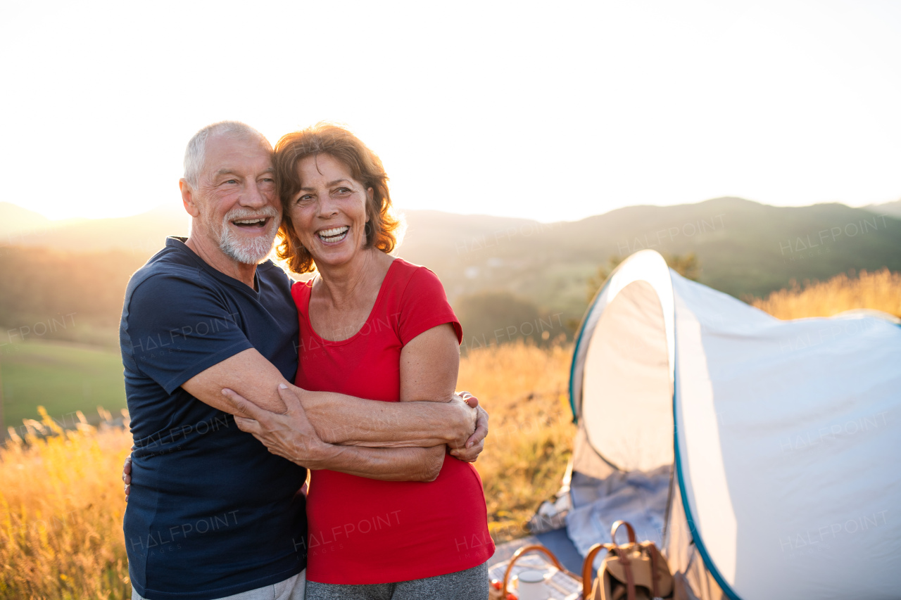 A senior tourist couple standing in nature at sunset, resting.