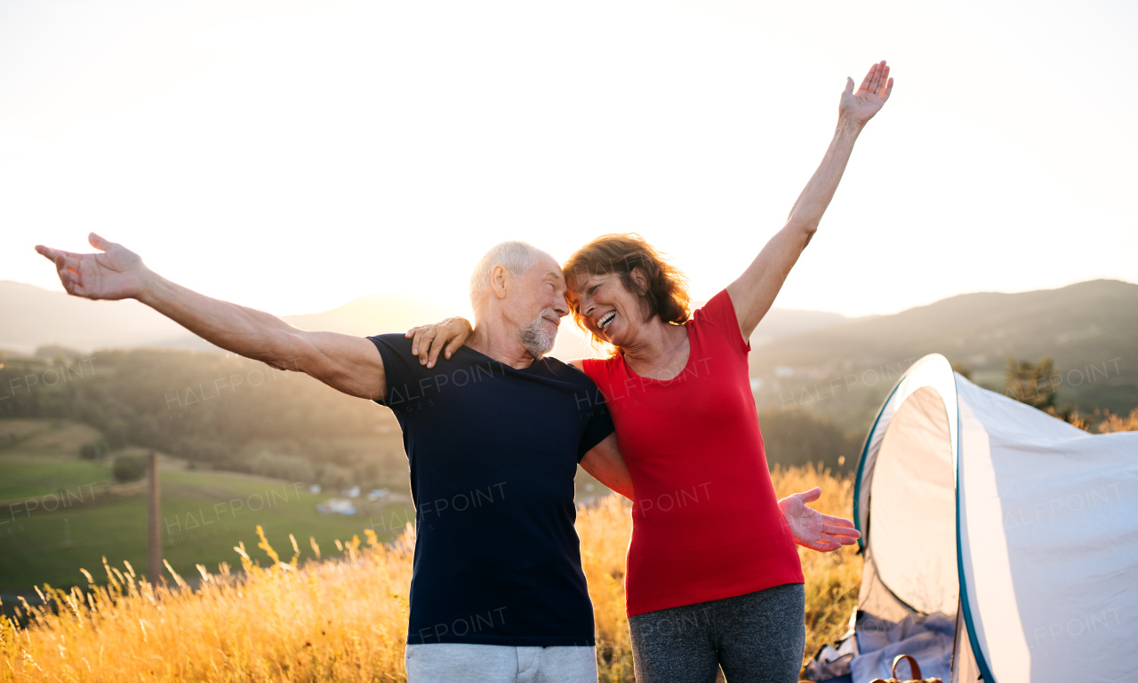 Front view of senior tourist couple travellers with backpacks hiking in nature, resting.