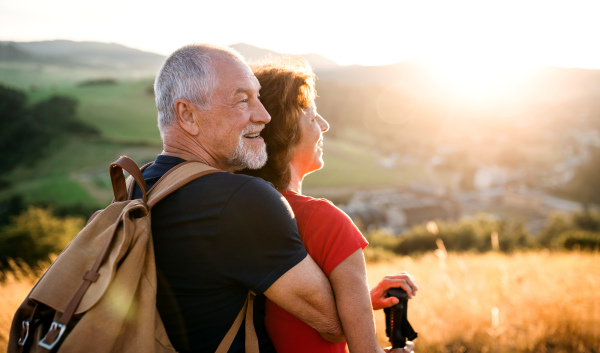 Senior tourist couple hikers with backpack standing in nature at sunset, resting. Copy space.