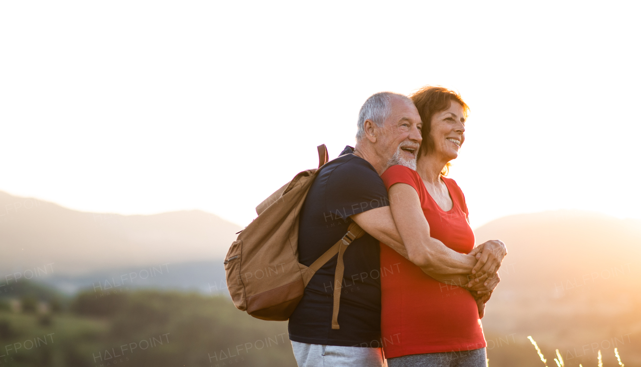 A side view of senior tourist couple hikers with backpacks standing in nature.