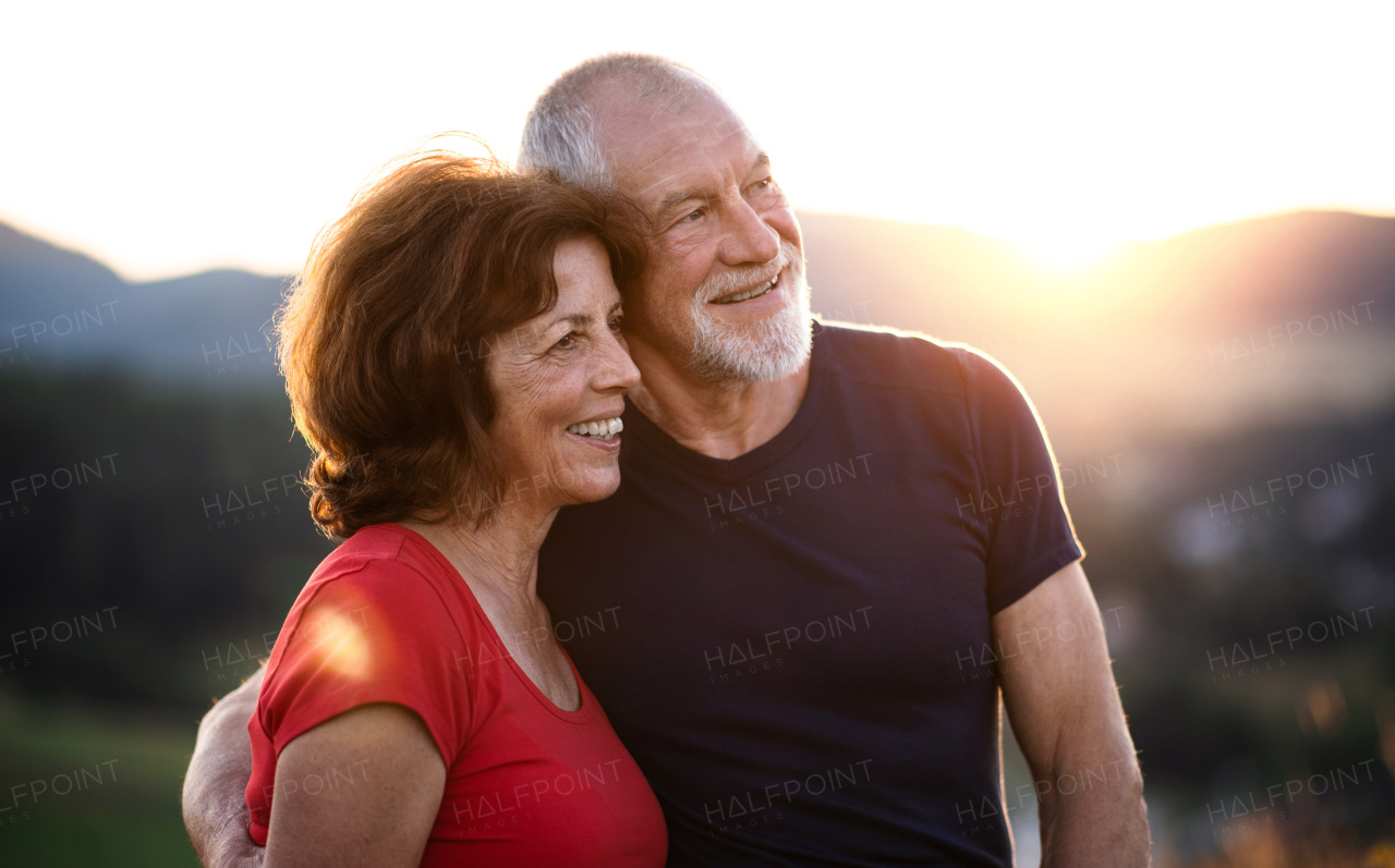 A senior tourist couple travellers with backpacks hiking in nature at sunset, resting. Copy space.