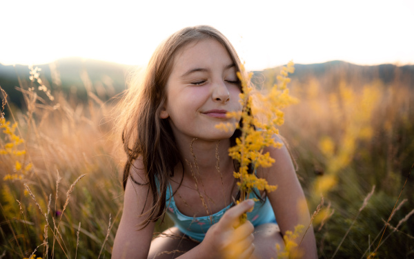 A portrait of happy small girl in grass in nature, holding flower.