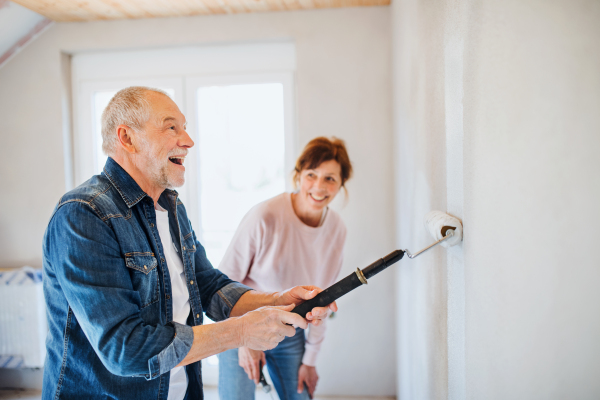 Happy senior couple painting walls in new home, relocation concept.