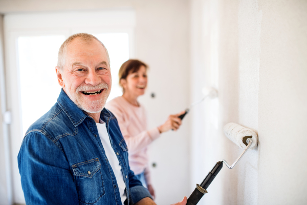 Happy senior couple painting walls in new home, relocation concept.