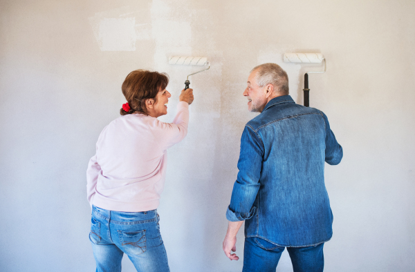 Rear view of happy senior couple painting walls in new home, relocation concept.