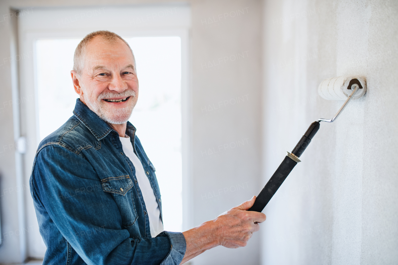 Portrait of cheerful senior man painting walls in new home, having fun. Relocation concept.