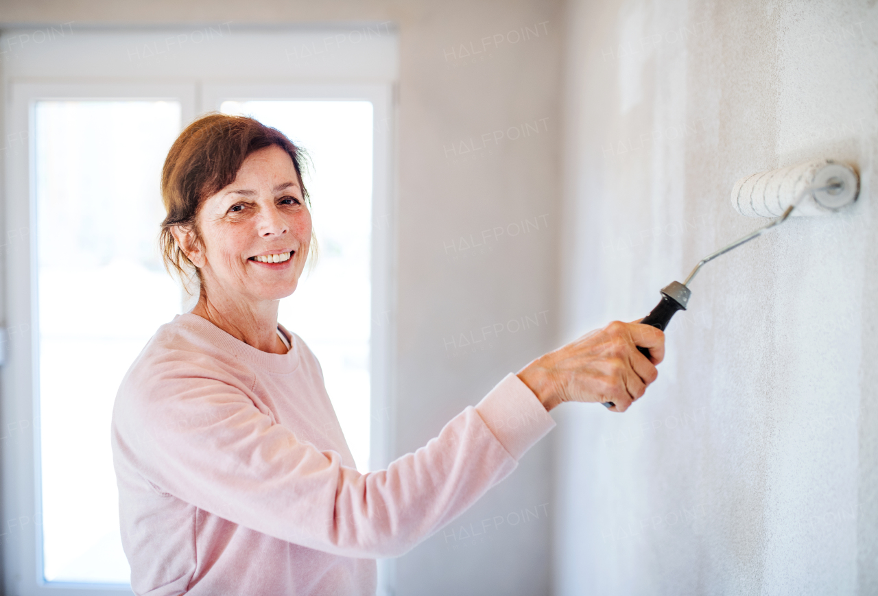 Portrait of cheerful senior woman painting walls in new home, having fun. Relocation concept.