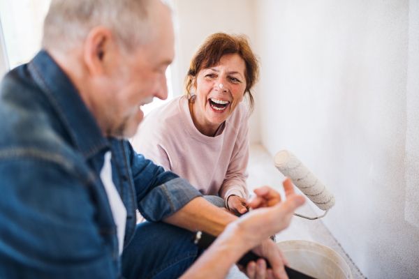 Happy senior couple painting walls in new home, relocation concept.