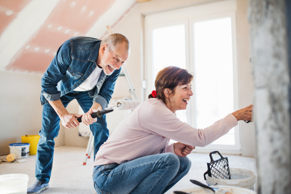 Happy senior couple painting walls in new home, relocation concept.