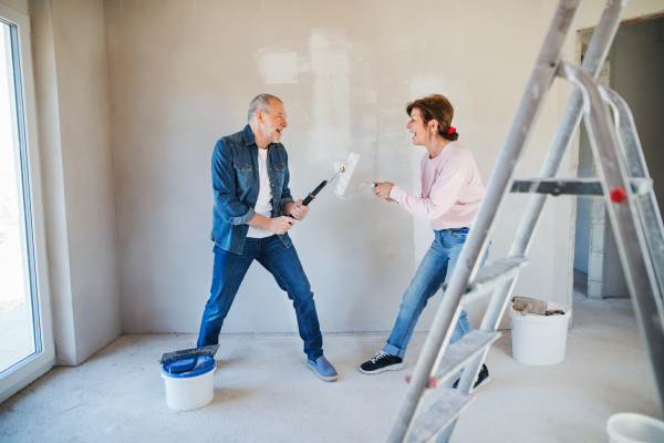 Portrait of cheerful senior couple painting walls in new home, having fun. Relocation concept.