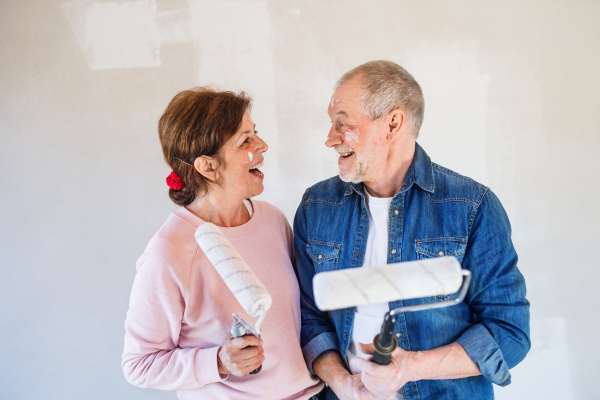 Portrait of cheerful senior couple painting walls in new home, having fun. Relocation concept.