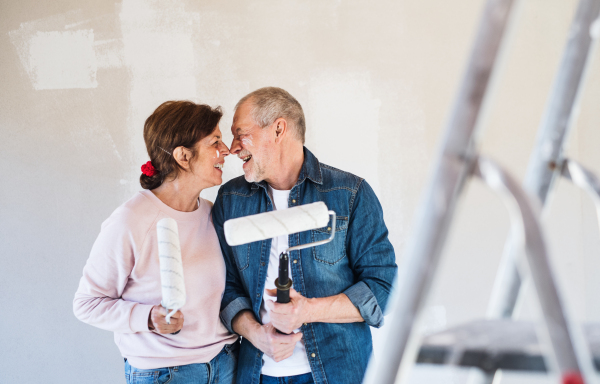 Happy senior couple painting walls in new home, having fun. Relocation concept.