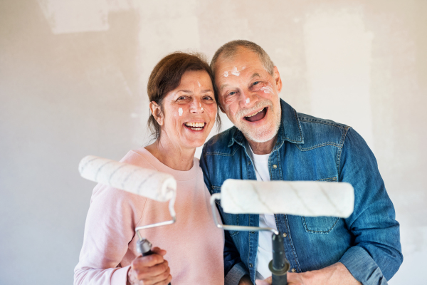 Portrait of cheerful senior couple painting walls in new home, having fun. Relocation concept.