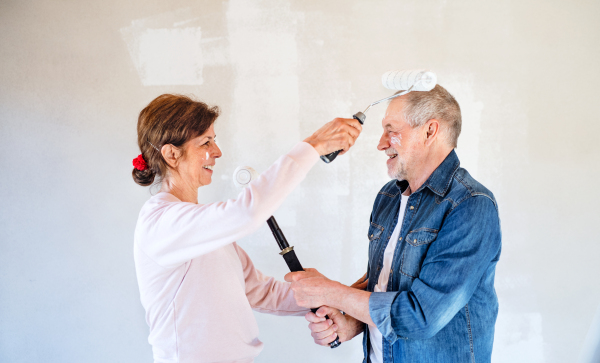 Happy senior couple painting walls in new home, having fun. Relocation concept.