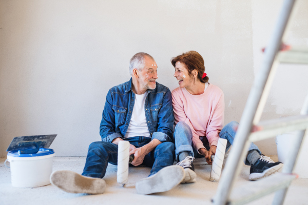 Portrait of cheerful senior couple painting walls in new home, resting. Relocation concept.