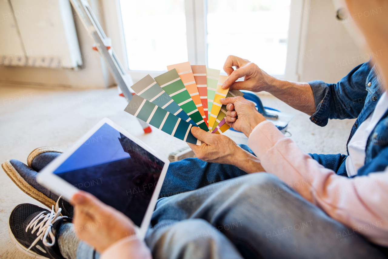 Senior couple with tablet painting new home, looking at color swatch. A relocation concept.