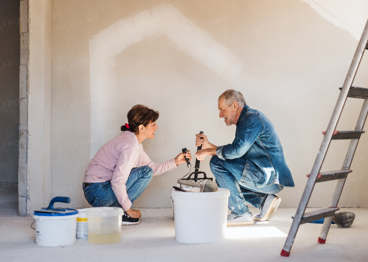 Happy senior couple painting walls in new home, relocation concept.