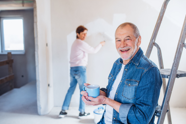 Happy senior couple painting walls in new home, relocation concept.