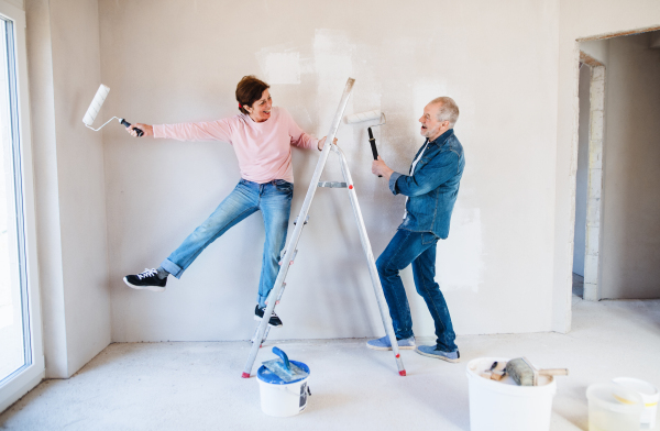 Portrait of cheerful senior couple painting walls in new home, having fun. Relocation concept.