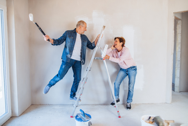 Portrait of cheerful senior couple painting walls in new home, having fun. Relocation concept.