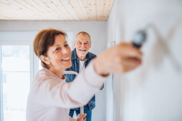 Happy senior couple painting walls in new home, relocation concept.