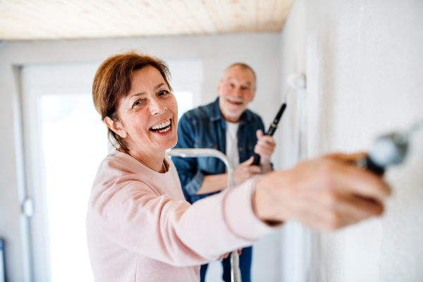 Happy senior couple painting walls in new home, relocation concept.