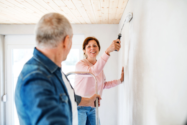 Happy senior couple painting walls in new home, relocation concept.