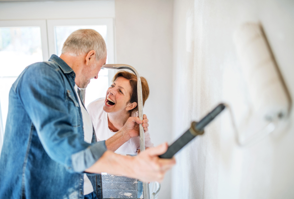 Happy senior couple painting walls in new home, relocation concept.