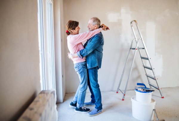 Portrait of cheerful senior couple painting walls in new home, hugging. Relocation concept.