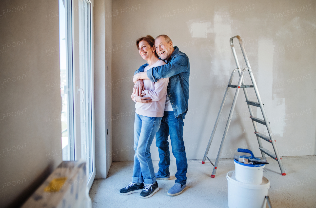 Portrait of cheerful senior couple painting walls in new home, resting. Relocation concept.