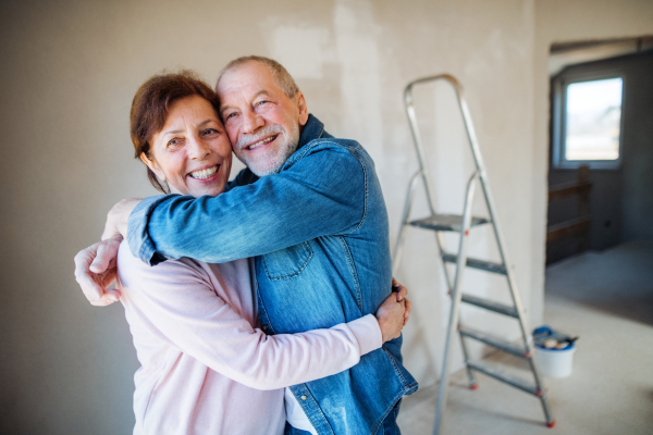 Portrait of cheerful senior couple painting walls in new home, hugging. Relocation concept.